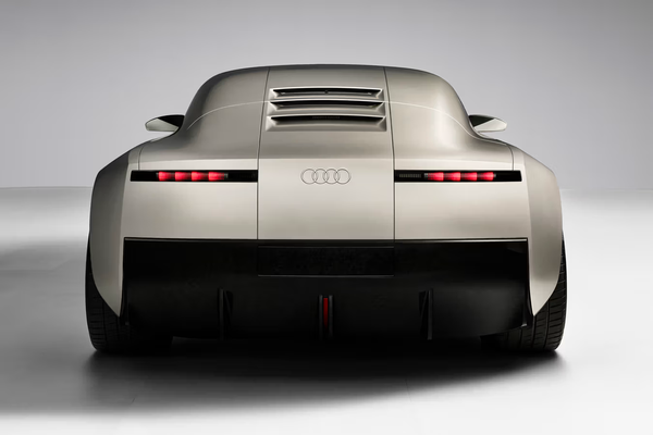 A matte silver metal bodied car, from behind, quite monolithic, in a white seamless room.